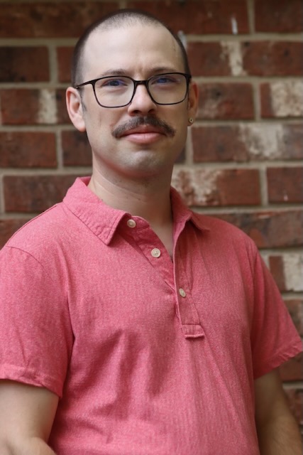 A self portrait of Cristóbal Palmer in front of a brick wall. I am a man with short hair and glasses wearing a short-sleeved collared shirt and viewed from the waist up